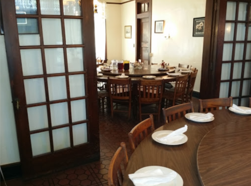A cozy dining room with a large round table set for a meal, surrounded by wooden chairs and warm lighting.
