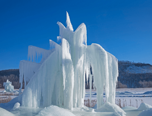 A striking ice formation with sharp, jagged edges against a clear blue sky and snowy landscape.