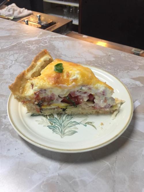 A slice of quiche on a decorative plate, featuring a golden crust and a filling of tomatoes and cheese.
