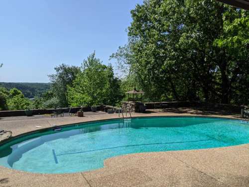A clear blue swimming pool surrounded by greenery and a scenic view on a sunny day.