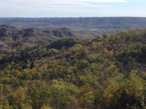 A scenic view of rolling hills and valleys, with trees displaying autumn colors under a clear blue sky.