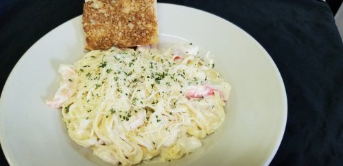 A plate of creamy pasta with shrimp, topped with parsley and grated cheese, accompanied by a slice of toasted bread.