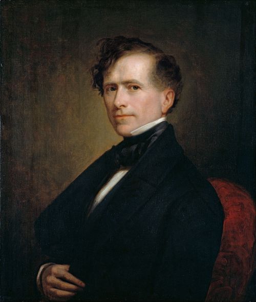 Portrait of a man in a formal suit with a bow tie, gazing confidently to the side against a dark background.
