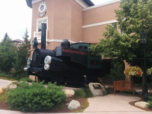 A vintage steam locomotive displayed outside a building, surrounded by greenery and decorative flowers.