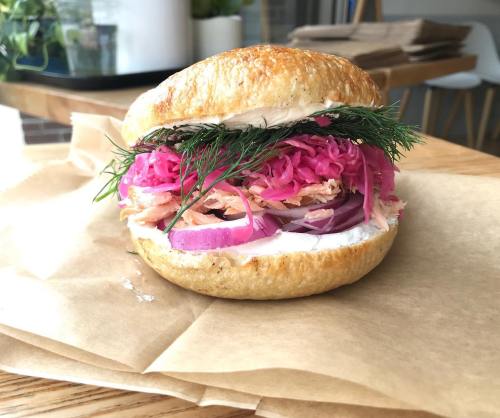 A bagel filled with cream cheese, smoked salmon, pink pickled cabbage, red onion, and fresh dill on a wooden table.