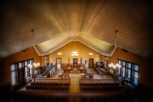 A spacious, historic courtroom with high ceilings, wooden benches, and a judge's bench at the front.