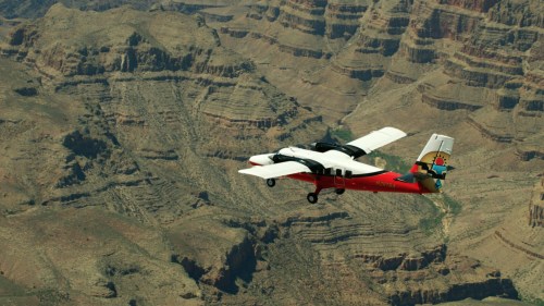 A small aircraft flying over the rugged terrain of the Grand Canyon, showcasing its layered rock formations.