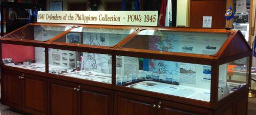 Display case showcasing the "1941 Defenders of the Philippines Collection - POWs 1945" with maps and photographs.