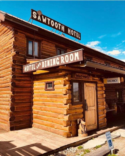 Log cabin-style building with a sign reading "Sawtooth Hotel" and "Hotel and Dining Room," featuring a wooden door.