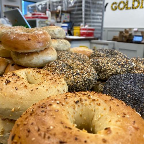 A variety of freshly baked bagels, including sesame and everything bagels, stacked on a display.