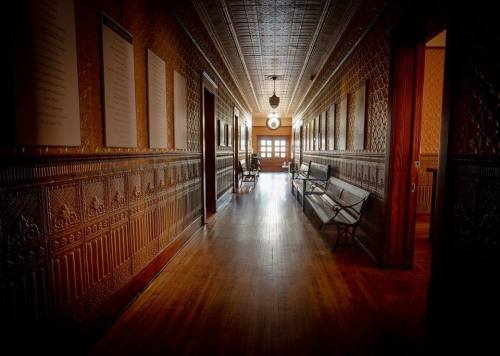 A long, ornate hallway with wooden floors, benches, and decorative walls, illuminated by a central light fixture.