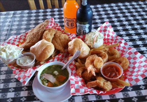A table with two plates of fried seafood, coleslaw, fries, and drinks, all on a checkered tablecloth.