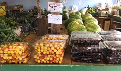 Fresh produce display at a market featuring yellow and red cherries, with watermelons in the background.