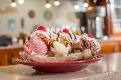 A colorful banana split with scoops of pink, yellow, and brown ice cream, topped with whipped cream and cherries.