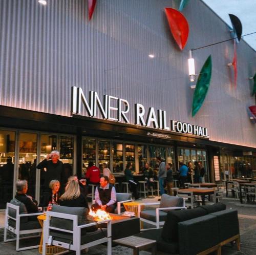 A lively food hall with outdoor seating, people socializing, and colorful decorations in the background.