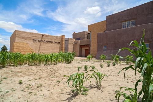 Sky City Cultural Center with adobe-style buildings and a field of corn in the foreground under a blue sky.