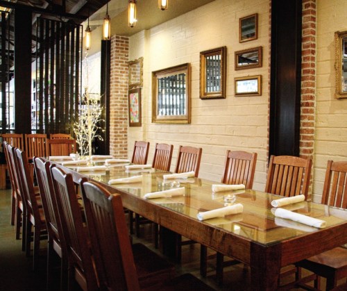 A spacious dining area with a long wooden table, surrounded by chairs and decorated with framed art on the walls.