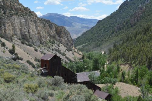 A rustic building nestled in a valley surrounded by mountains and lush greenery under a partly cloudy sky.