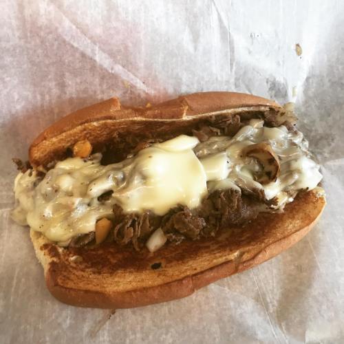 A toasted sandwich filled with sliced beef, melted cheese, and sautéed onions on a paper wrapper.