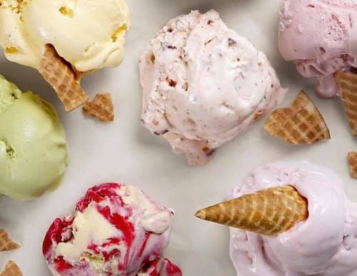 A variety of colorful ice cream scoops with waffle cone pieces on a light background.