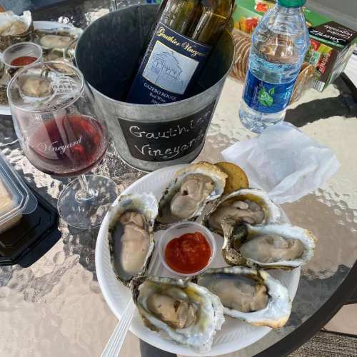 A plate of oysters with cocktail sauce, a glass of red wine, and a bottle of white wine on a table.