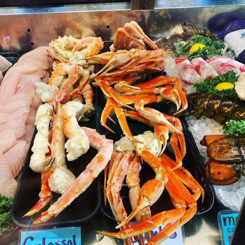A display of fresh seafood, including crab legs, lobster, and various fish fillets on ice with garnishes.