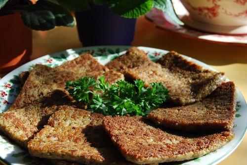 A plate of golden-brown, crispy slices of food garnished with fresh parsley, set on a colorful table.
