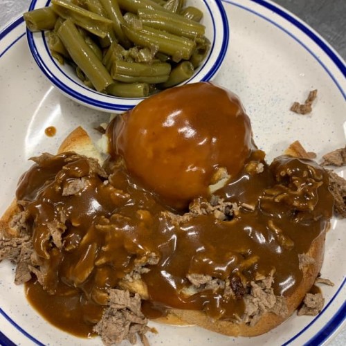 A plate with sliced bread topped with beef and gravy, accompanied by a bowl of green beans.