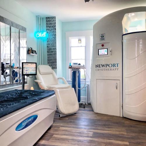 A modern cryotherapy room featuring a treatment bed, cryotherapy machine, and a neon "Chill" sign on the wall.