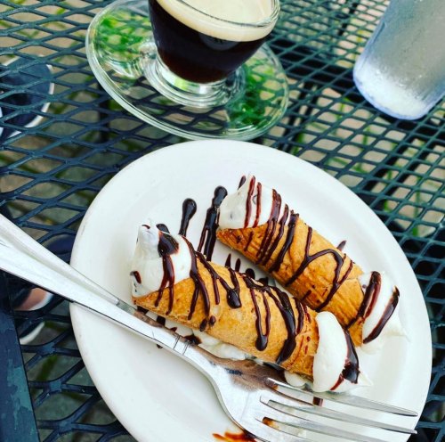 Two cannoli drizzled with chocolate sauce on a white plate, accompanied by a small glass of espresso.