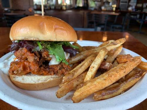 A crispy fried chicken sandwich with lettuce and sauce, served with a side of golden fries on a paper plate.
