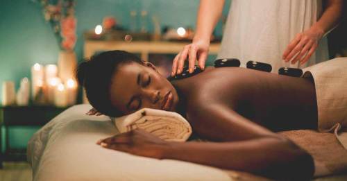 A woman receiving a hot stone massage in a serene spa setting, with candles and soft lighting in the background.