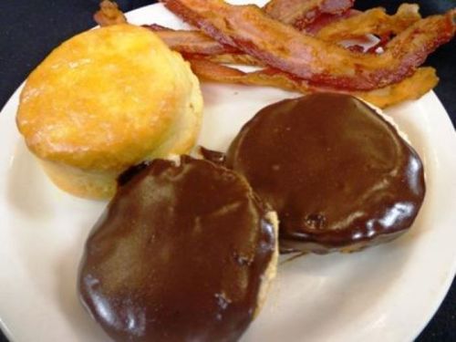 A plate with a biscuit, two chocolate-covered pastries, and crispy bacon strips.