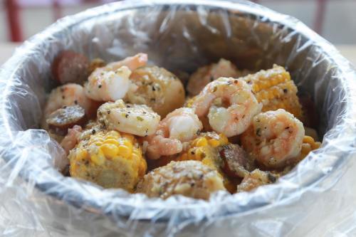 A bowl filled with shrimp, corn, and sausage, covered in spices and wrapped in plastic.