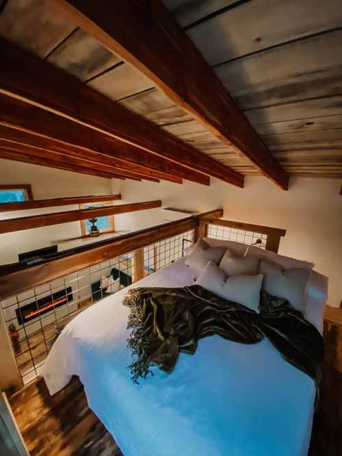 Cozy loft bedroom with a wooden ceiling, a large bed adorned with pillows and a blanket, and a warm ambiance.