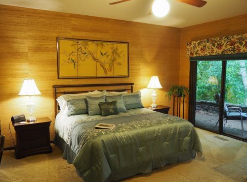 Cozy bedroom with a king-sized bed, bamboo wall decor, two lamps, and a sliding glass door leading to a patio.