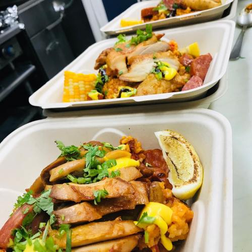 Three food trays filled with rice, grilled meats, corn, and garnished with herbs and lemon wedges.