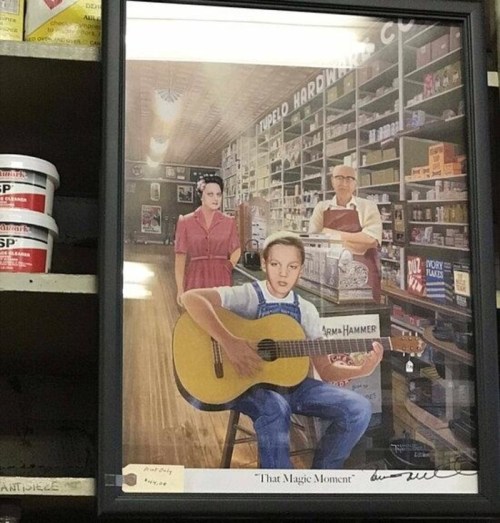 A framed artwork featuring a girl playing guitar in a store, with two figures in the background among shelves.