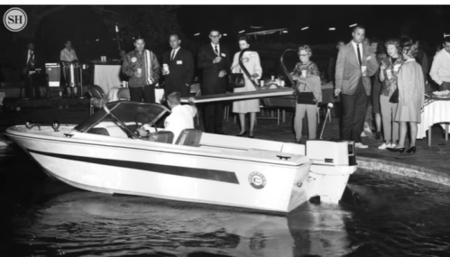A group of people watches as a man operates a small boat near a poolside gathering in a vintage setting.