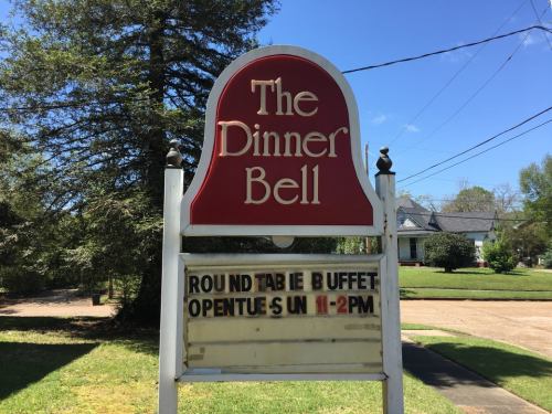Sign for "The Dinner Bell" restaurant featuring a round table buffet, open Sundays from 11 AM to 2 PM.