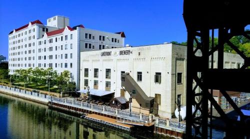 Historic brewery building by a river, featuring a modern hotel with a red-roofed design and outdoor seating area.