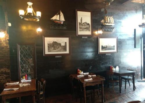 Cozy restaurant interior with wooden tables, vintage ship paintings, and warm lighting on dark wooden walls.