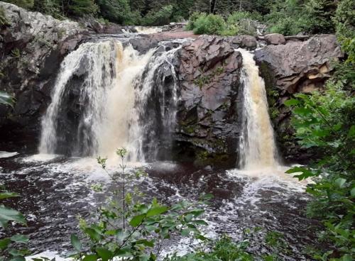 A scenic waterfall cascading over rocky cliffs into a dark pool, surrounded by lush greenery.