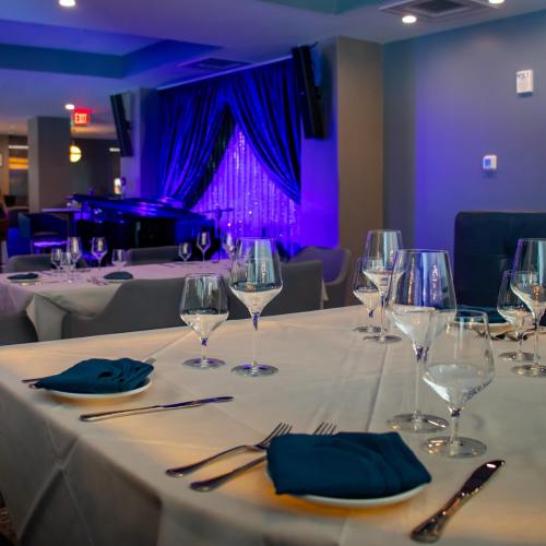 Elegant dining setup with blue accents, sparkling lights, and a piano in a stylish restaurant interior.