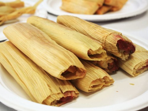 A plate of tamales wrapped in corn husks, showcasing their filling peeking out from the ends.