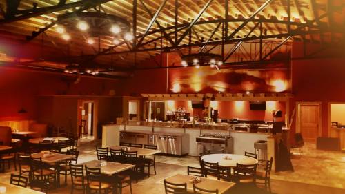 Interior of a cozy restaurant featuring wooden tables, a bar area, and warm lighting with an industrial ceiling design.