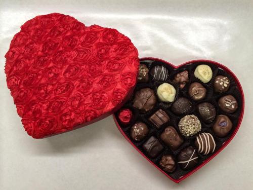 A heart-shaped box with a red rose design, filled with assorted chocolates.