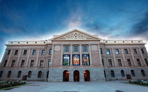 Historic building with ornate architecture, featuring Arizona flags and a dramatic sky in the background.