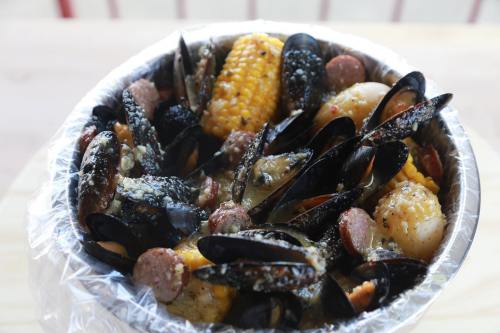 A bowl of seafood featuring mussels, corn, sausage, and spices, all cooked together in a flavorful broth.