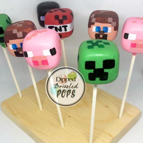 Colorful cake pops shaped like Minecraft characters, including a pig, creeper, and TNT, displayed on a wooden stand.